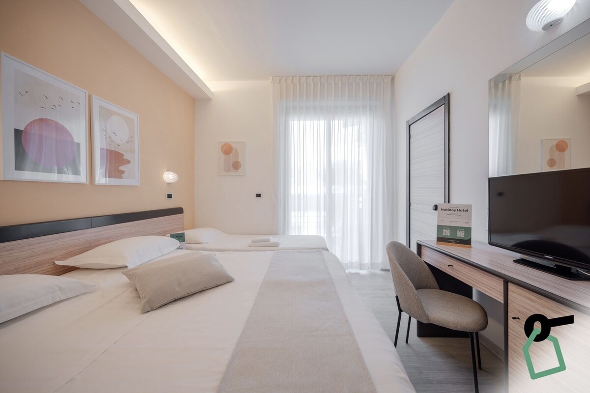 Une chambre d’hôtel avec deux lits, un bureau, une chaise, un téléviseur à écran plat et des œuvres d’art accrochées aux murs.