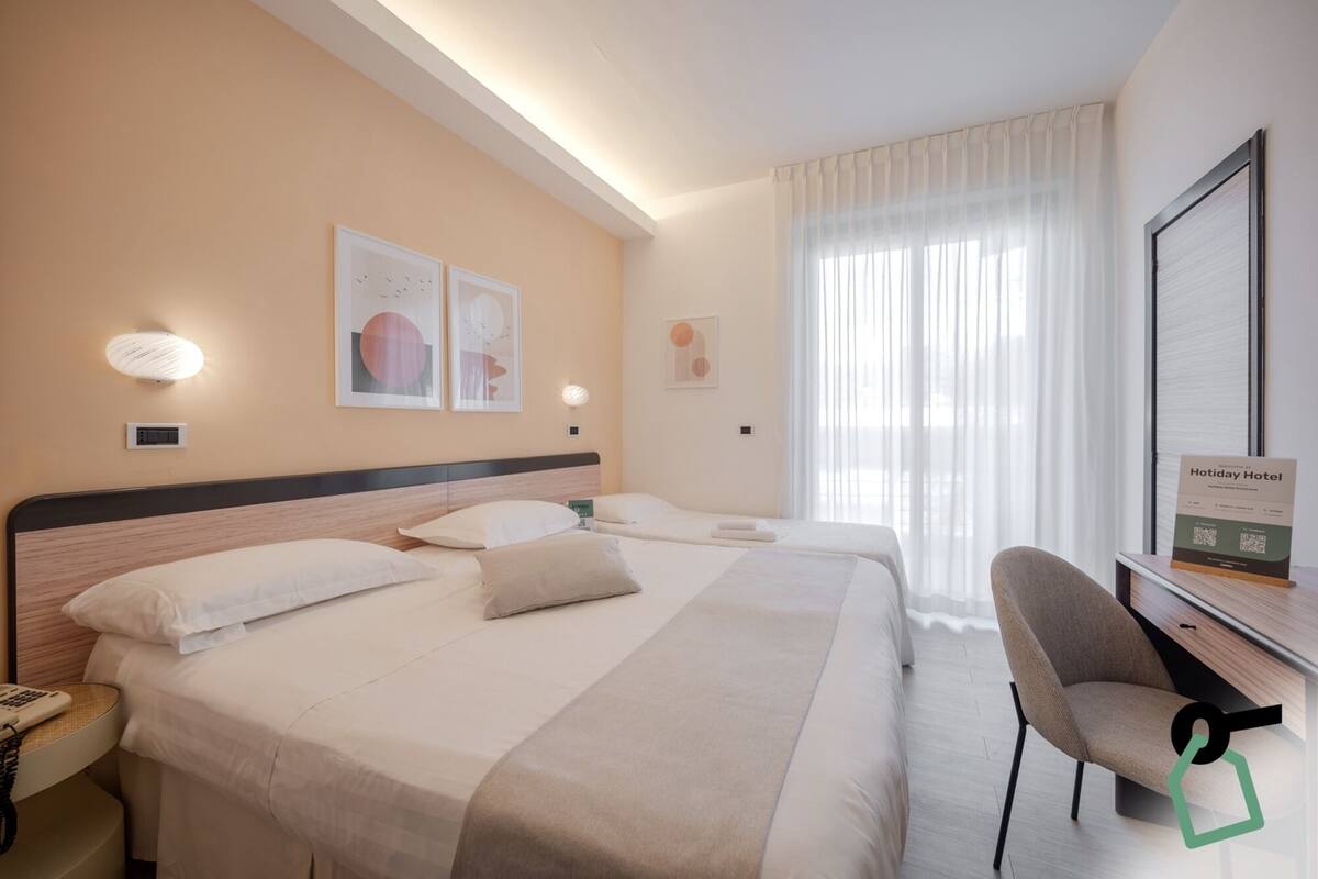 Een hotelkamer met twee bedden, een bureau, een stoel en kunstwerken aan de muur.