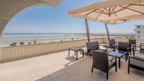 Ein Balkon mit Gartenmöbeln, Blick auf den Strand und einen klaren Himmel.