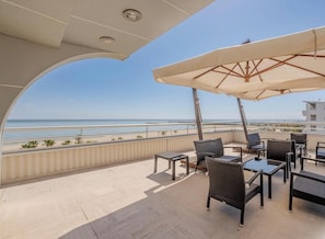 Un balcón con mobiliario exterior, vista a la playa y cielo despejado.