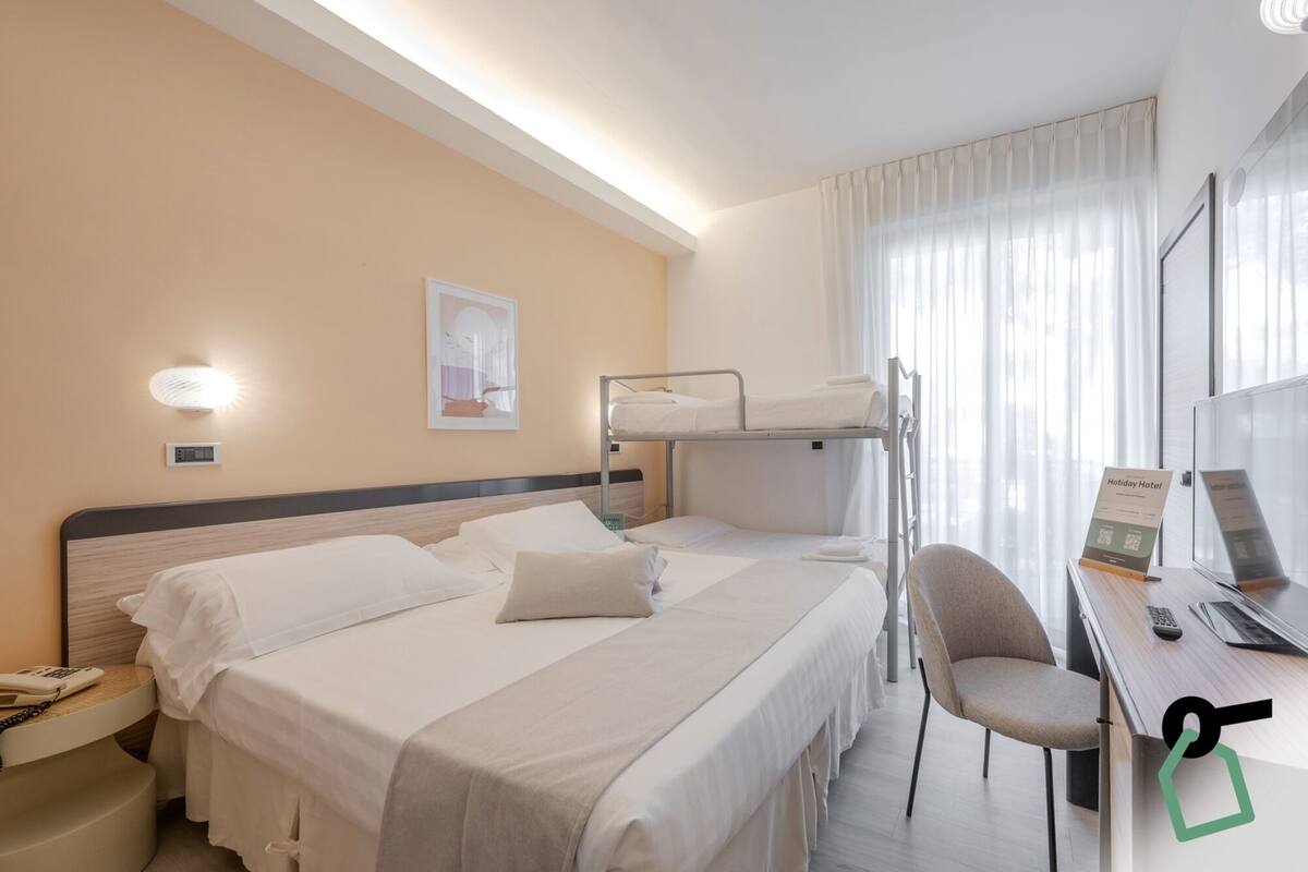 Een hotelkamer met een stapelbed, een bureau met een computer en een stoel.
