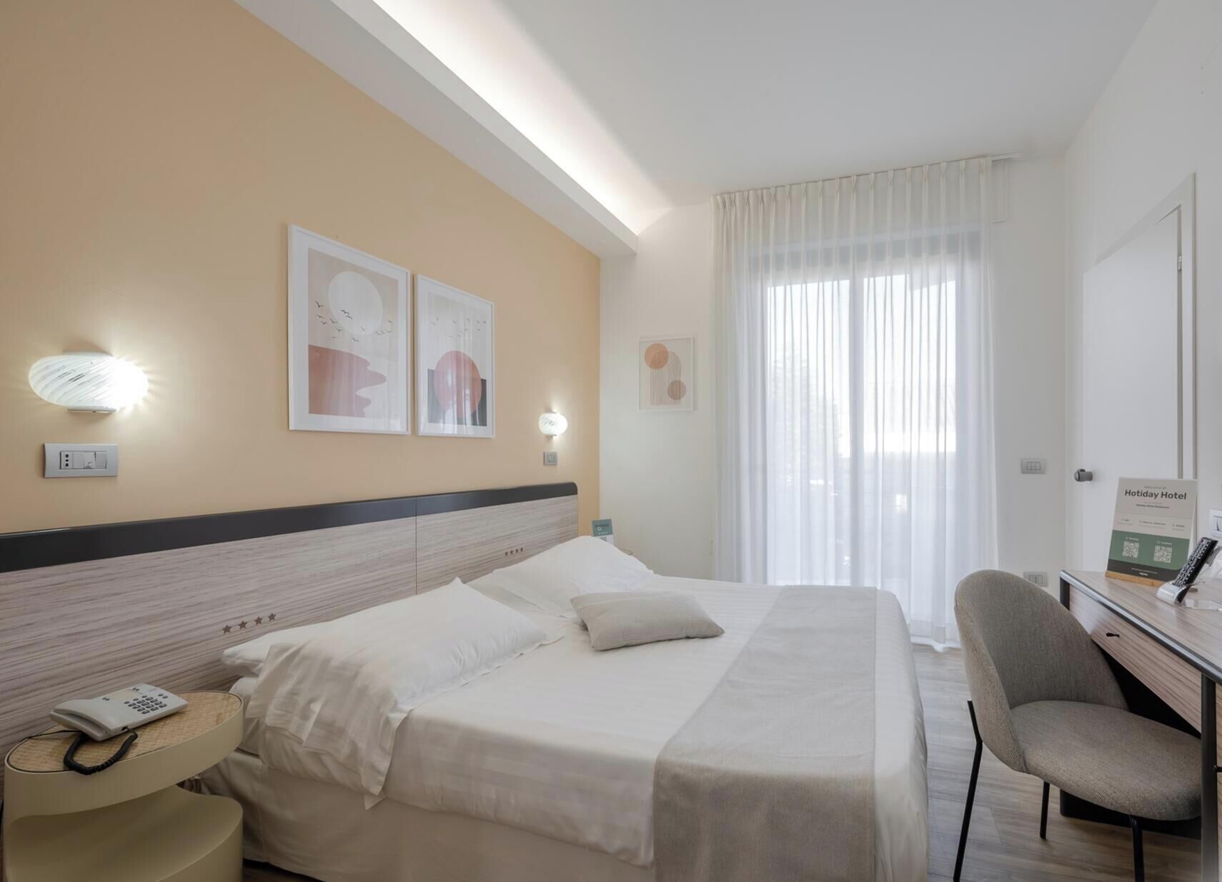 Een hotelkamer met een bed, nachtkastje, lamp en een bureau met stoel.