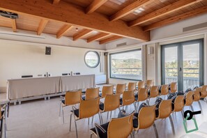 Uma sala de conferência com uma mesa comprida e cadeiras, grandes janelas com vista e vigas de madeira no teto.