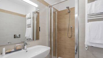 A modern bathroom with a glass shower enclosure, a white sink, and a towel rack.