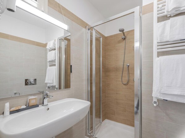 A modern bathroom with a glass shower enclosure, a white sink, and a towel rack.