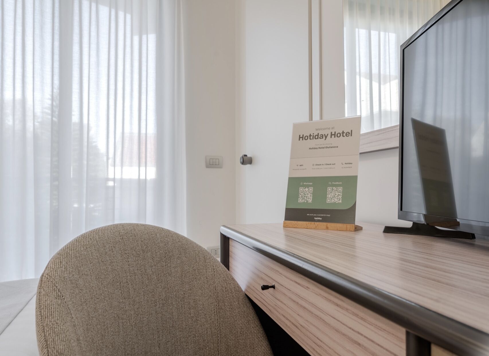 A hotel room with a wooden desk, a television, and a sign indicating the room number.