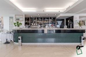 Uma área de bar com balcão, prateleiras cheias de garrafas de bebidas e uma máquina de café.