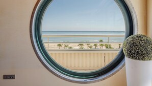 Una ventana redonda con vista a una playa y palmeras.