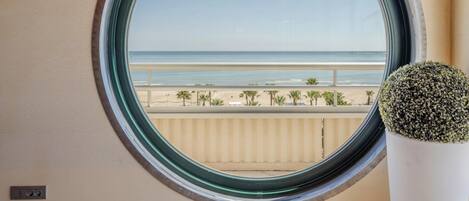 A round window with a view of a beach and palm trees.