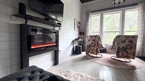 A modern living room with a fireplace, comfortable seating, and a large window.