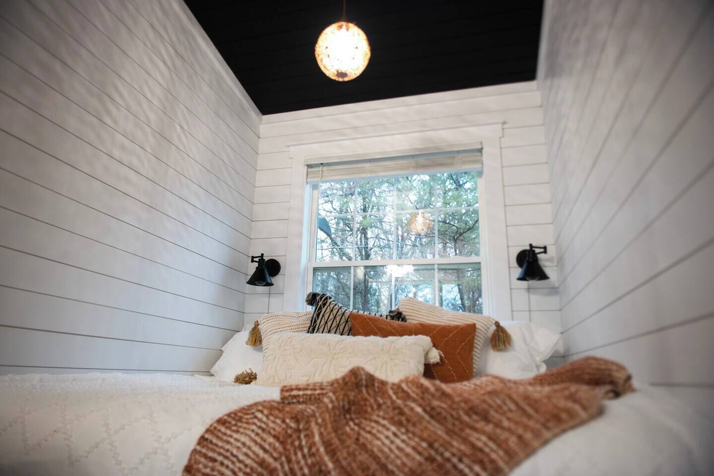 A cozy bedroom with a bed, pillows, and a window with a view of trees.