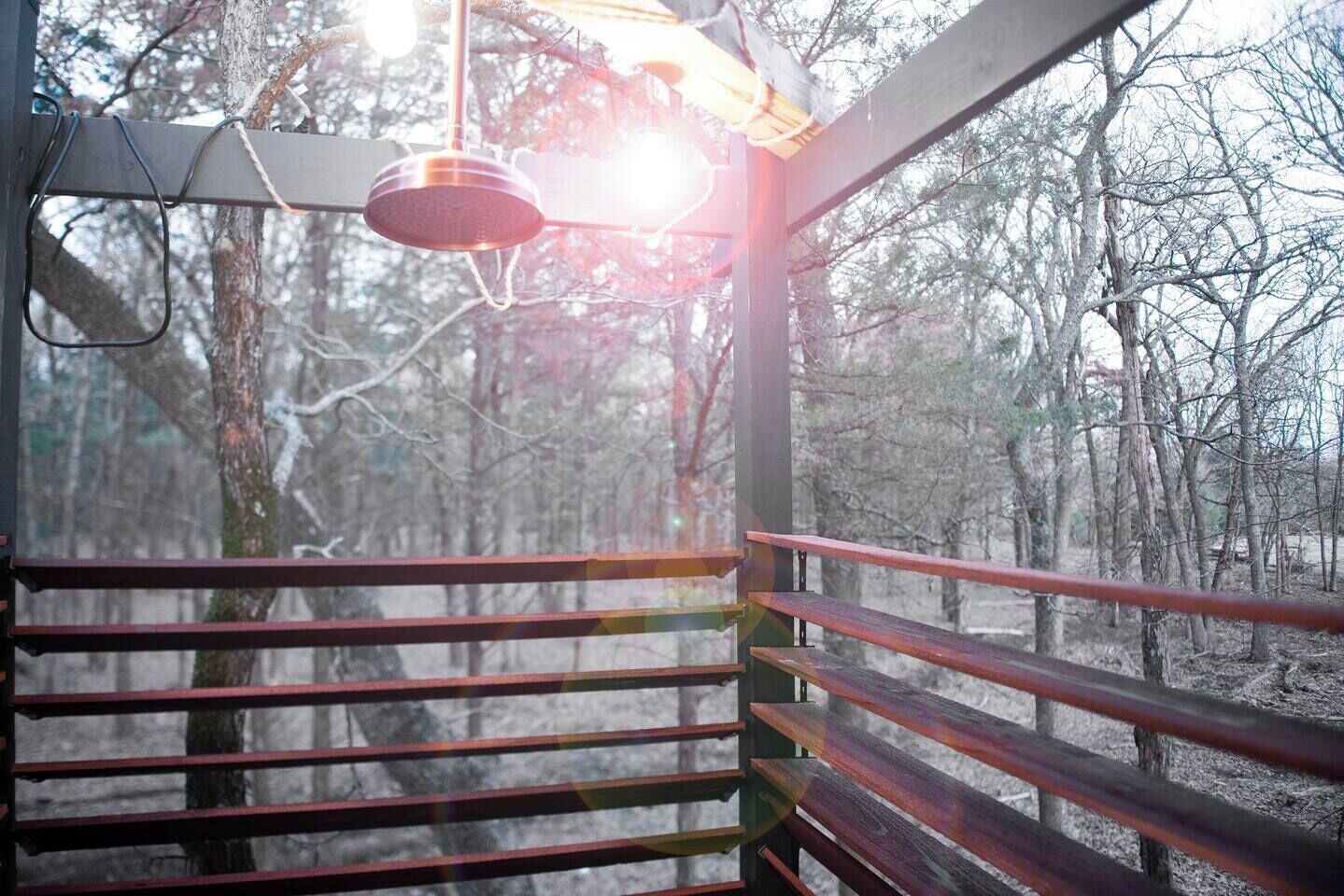Una terraza de madera con barandas metálicas, un colgante de luz y vistas a un área boscosa.