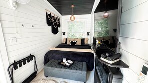 A compact bedroom with a bed, bedside table, and a small seating area. - Little Luxe Romantic Treehouse Cabin (Point)