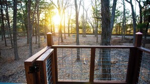 Une terrasse en bois avec une rambarde en métal donnant sur une zone boisée.