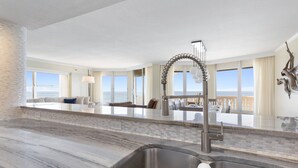 Una cocina moderna con una isla grande, pileta de acero inoxidable y vista al océano.
