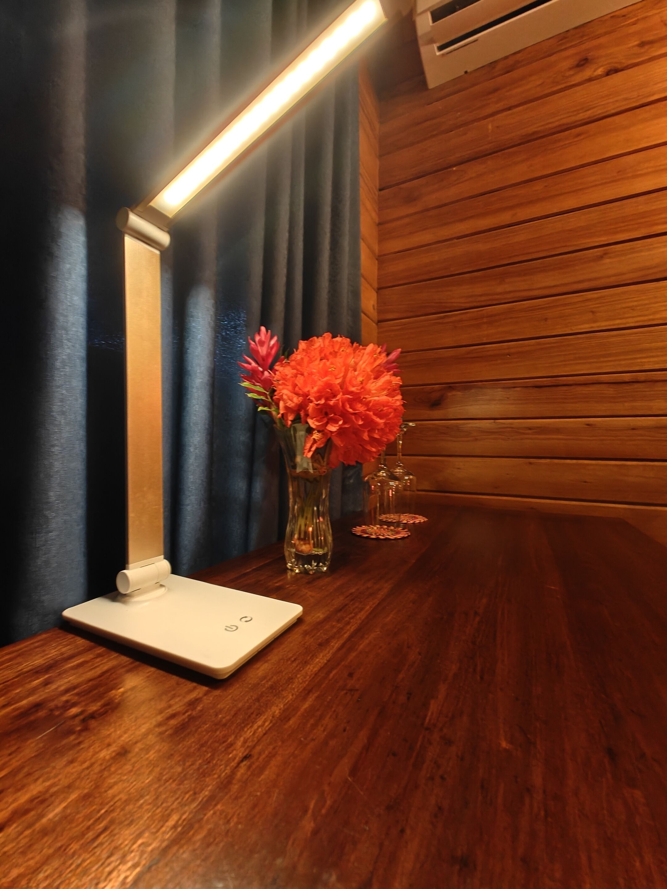 Una mesa de madera con un dispositivo blanco y un florero con flores naranjas.