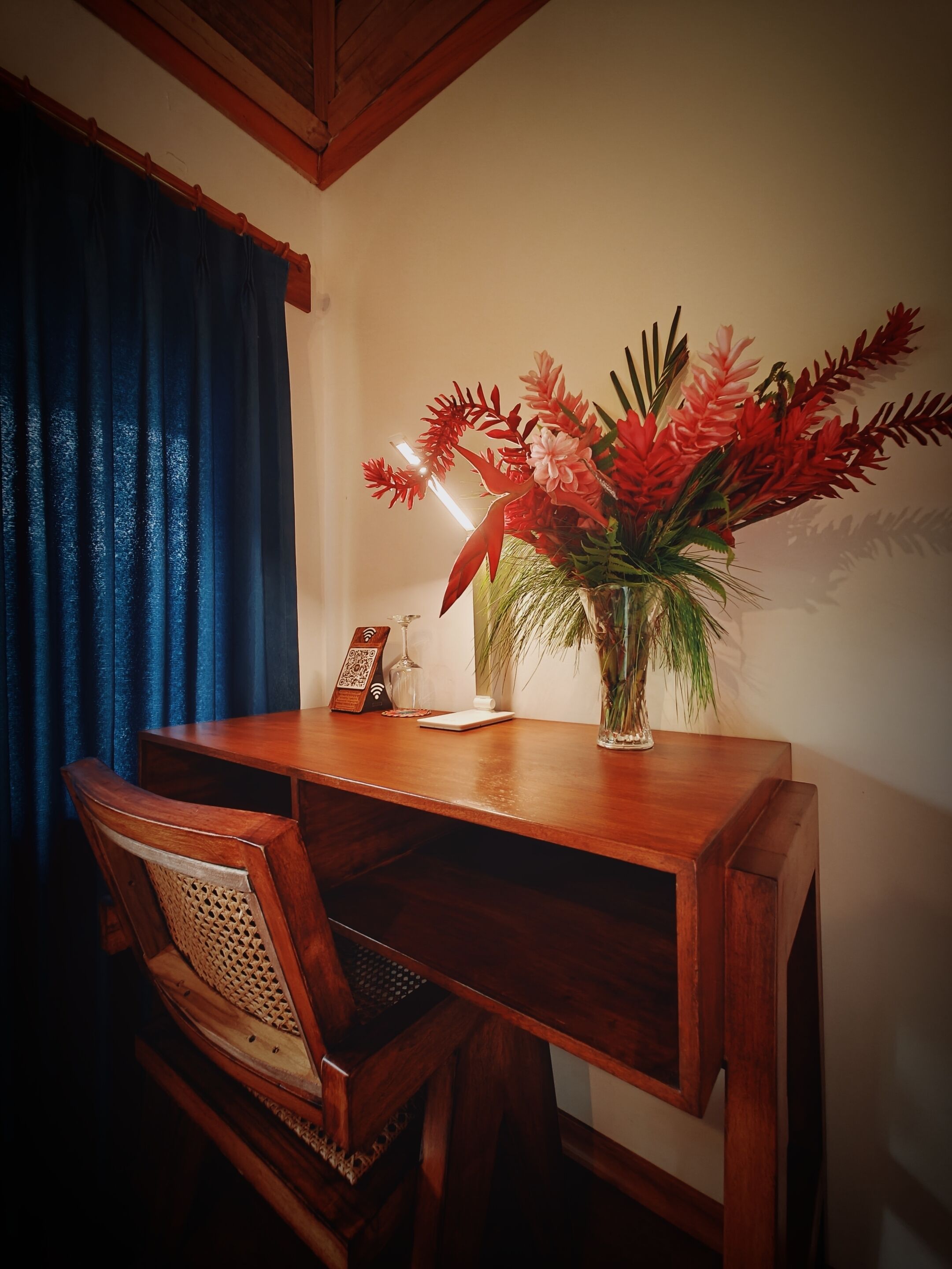 Escritorio de madera con un jarrón de flores rojas, un adorno pequeño y un vaso.