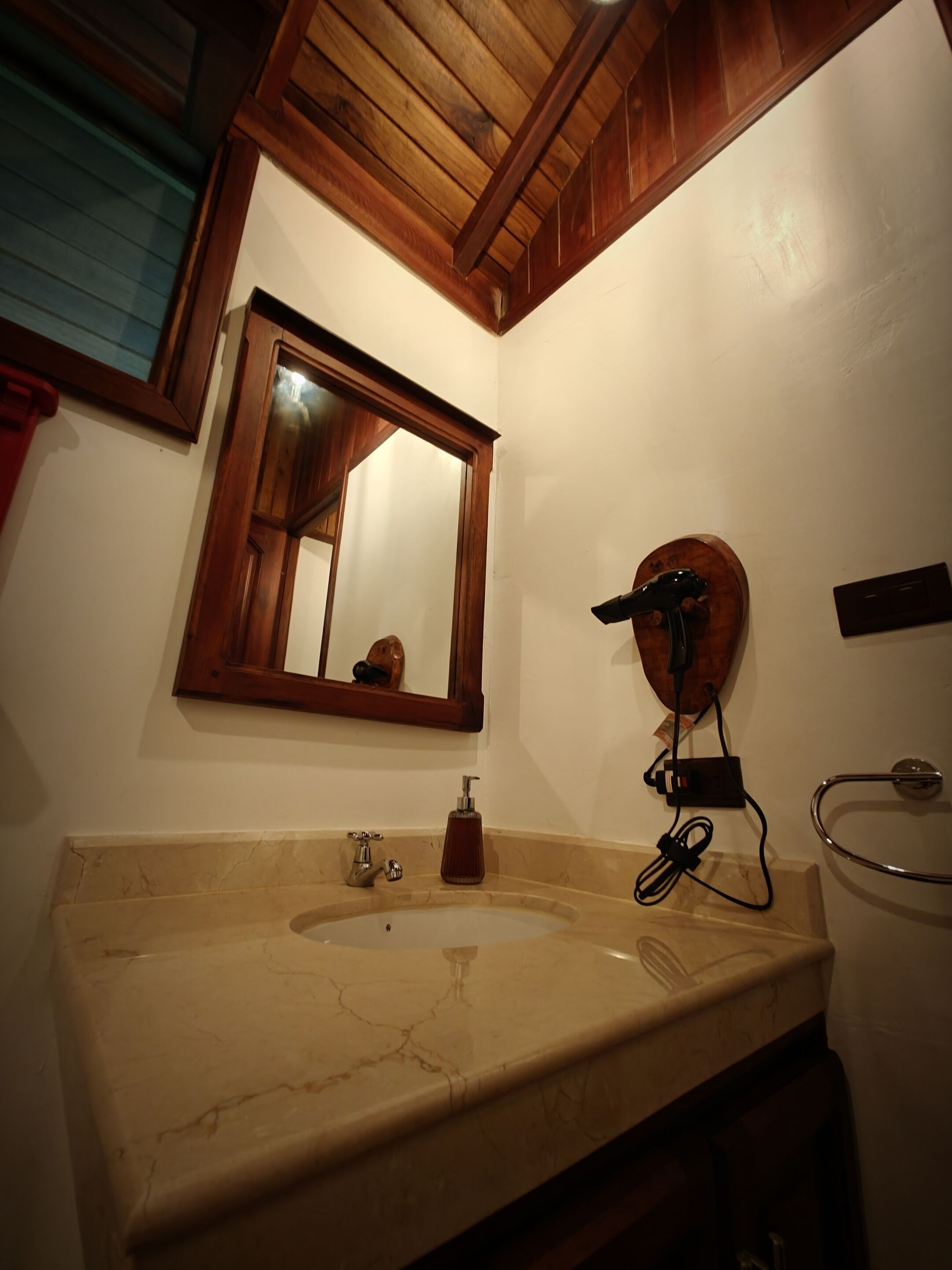 Un baño con lavamanos de mármol, vigas de techo de madera, un espejo y un perchero para toallas.