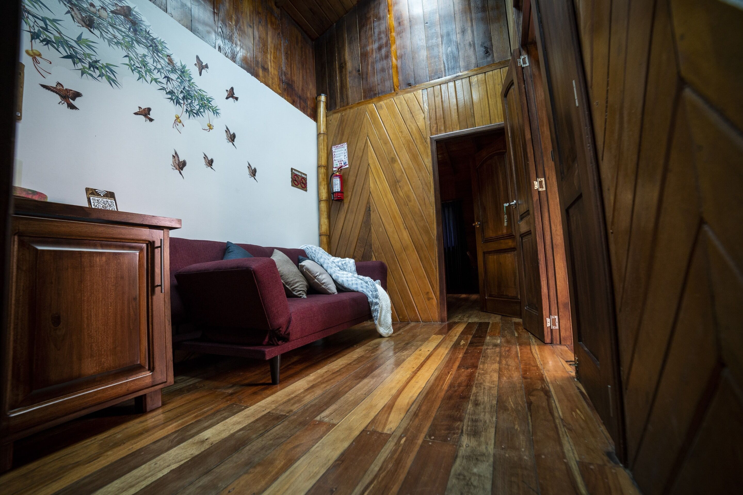 Un pasillo con suelo de madera, un sofá rojo y un armario.
