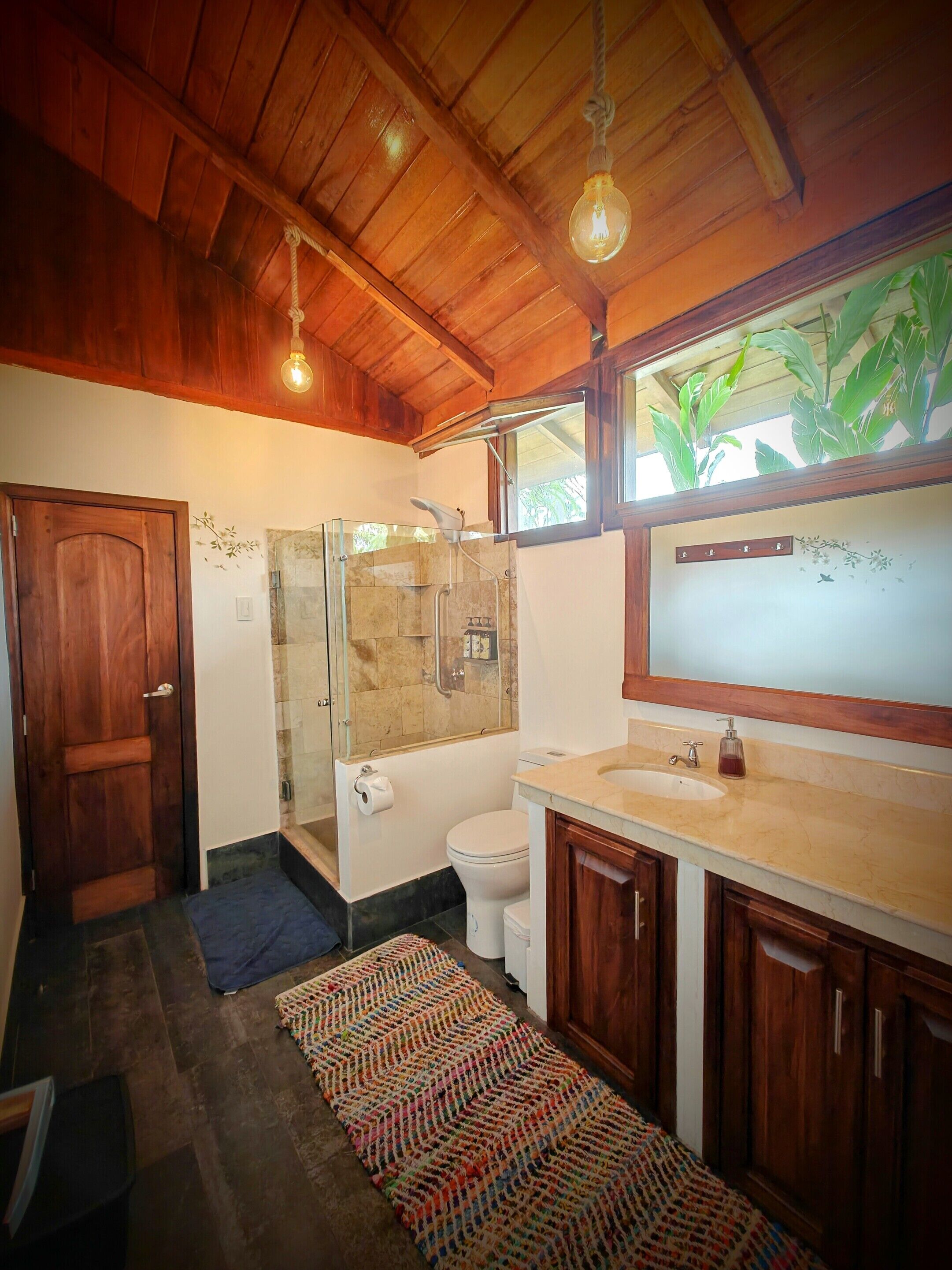 A bathroom with a wooden ceiling, a glass shower enclosure, a toilet, and a sink with a mirror.
