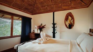 A bedroom with a wooden ceiling, a bed with white linens, a window with curtains, and a wall-mounted artwork.
