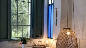 A room with a window, a hanging light fixture, a stool, and a small table with a plant and a bottle.