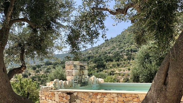 A serene outdoor seating area with a stone wall, a view of a hill, and a stone structure in the background.