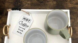 Ett bricka med två gröna muggar och en etikett med texten: ”Hett kaffe serveras färskt varje dag”.