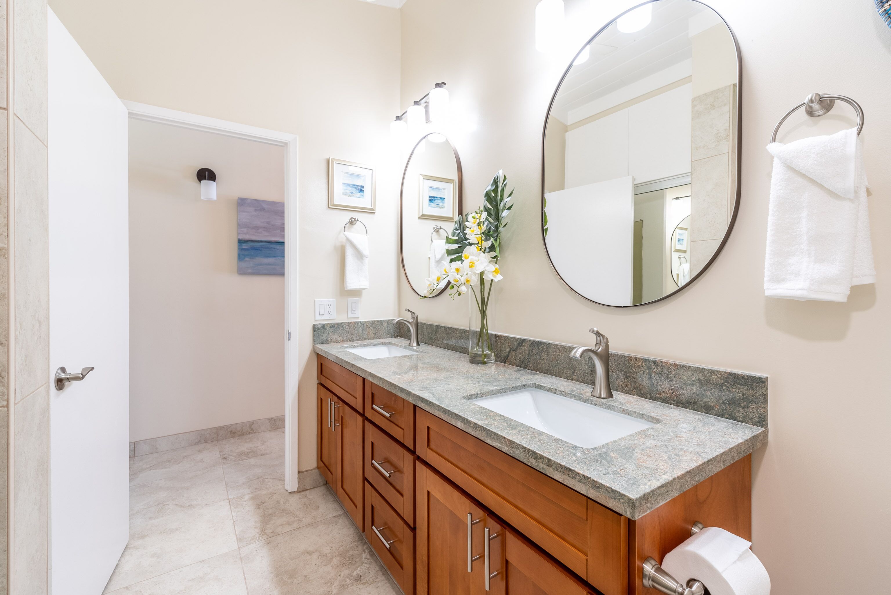 A bathroom with two sinks, wooden cabinets, a large mirror, and a toilet paper holder.