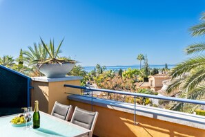 A balcony with a table, chairs, a bottle of champagne, and a potted plant. - Bahia de Marbella | Bright Beachside Apartment with Pool in Marbella (Marbella)