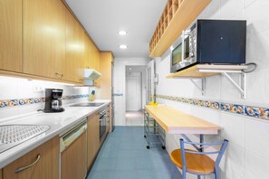 Una cucina piccola e stretta con mobili in legno, un forno a microonde, una macchina da caffè e un tavolino con una sedia.