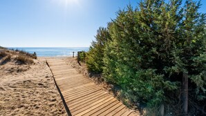 Un paseo marítimo de madera que conduce a una playa con cielos despejados y luz solar.