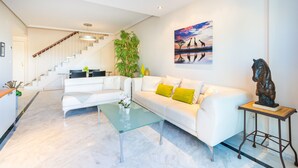 Una sala de estar moderna con un sofá blanco, una mesa de centro de vidrio y una escalera que lleva a otro nivel.