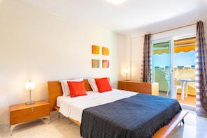 A bedroom with a bed, nightstands, a desk, and a view through a glass door. - Bahia de Marbella | Bright Beachside Apartment with Pool in Marbella (Marbella)