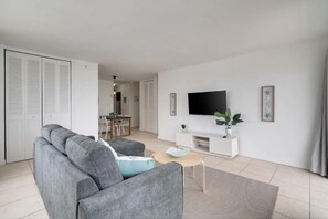 Uma sala de estar com um sofá cinzento, uma televisão, uma mesinha e uma planta.