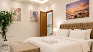 A modern bedroom with a large bed, a bedside table, a nightstand, a potted plant, and artwork on the walls. - Casa Rosa - المهندسين (Giza)