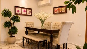 A dining area with a wooden table, four upholstered chairs, a bench, a potted plant, and two framed artworks on the wall. - Casa Rosa - المهندسين (Giza)