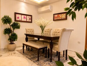A dining area with a wooden table, four upholstered chairs, a bench, a potted plant, and two framed artworks on the wall. - Casa Rosa - المهندسين (Giza)