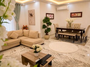 Una sala moderna con un sofá beige, una mesa de comedor con sillas, una mesa de centro con un control remoto y una planta en maceta.