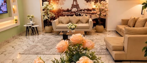 A living room with a sofa, a coffee table, and a TV. There is a mural of the Eiffel Tower and a painting on the wall.