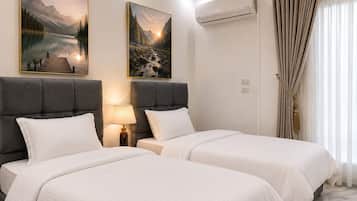 Habitación de hotel con dos camas, una mesita de noche con lámpara, un equipo de aire acondicionado y dos cuadros con paisajes en la pared.