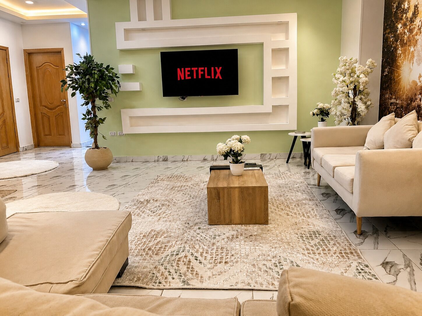 A modern living room with a flat-screen TV mounted on a white wall, a beige sofa, a coffee table, and a potted plant.
