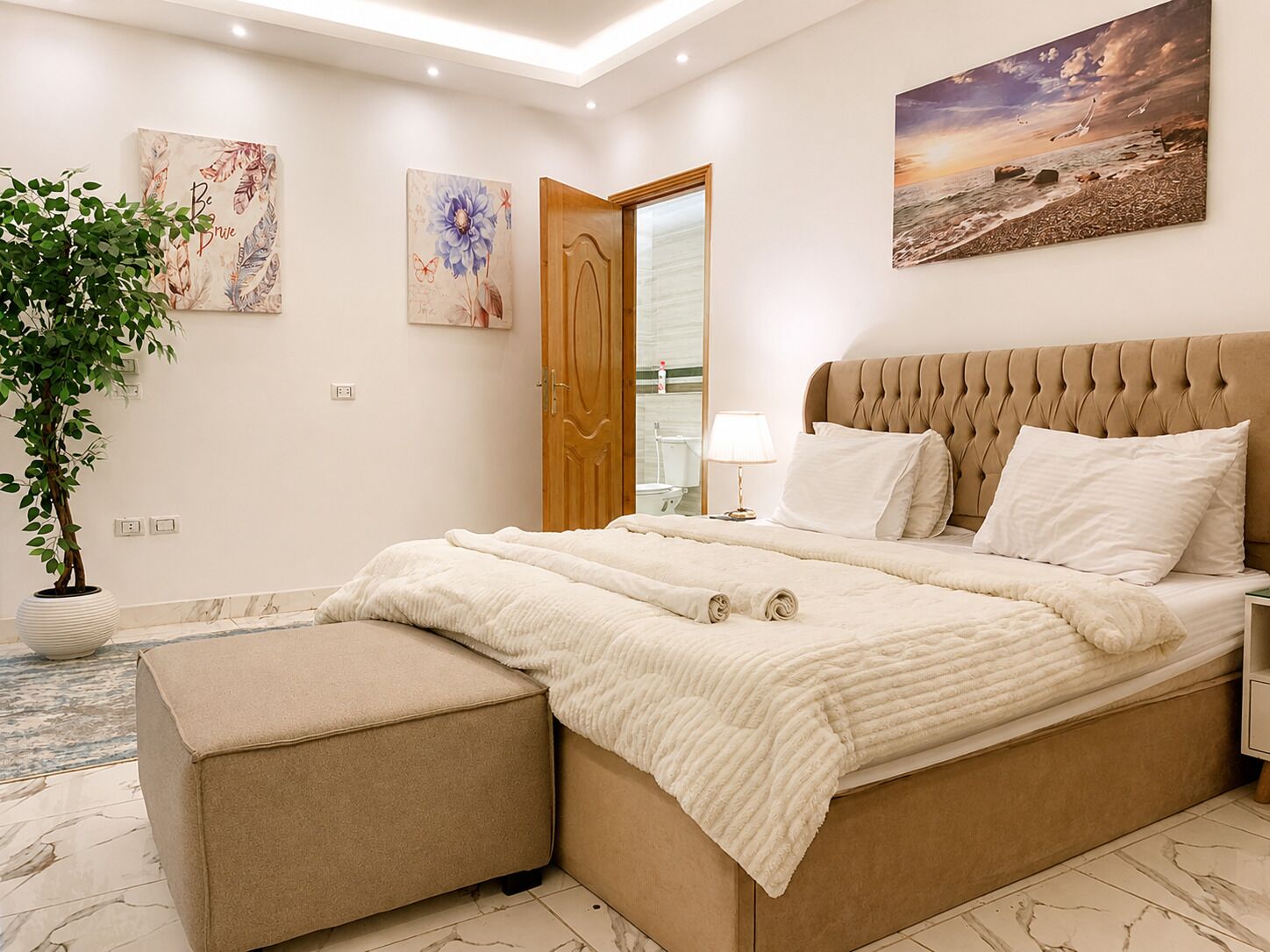 Een slaapkamer met een groot bed, een nachtkastje, een lamp en een schilderij aan de muur.