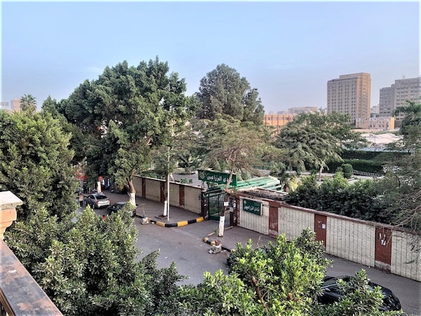 A gated parking area with a green sign, surrounded by trees and buildings in the background. - Casa Rosa - المهندسين (Giza)