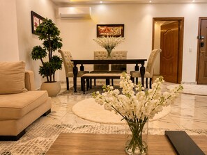 A living room with a sofa, a dining table with chairs, a potted plant, and a vase with flowers. - Casa Rosa - المهندسين (Giza)