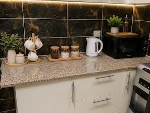A kitchen with a granite countertop, a microwave, a kettle, and various jars on the counter. - Casa Rosa - المهندسين (Giza)