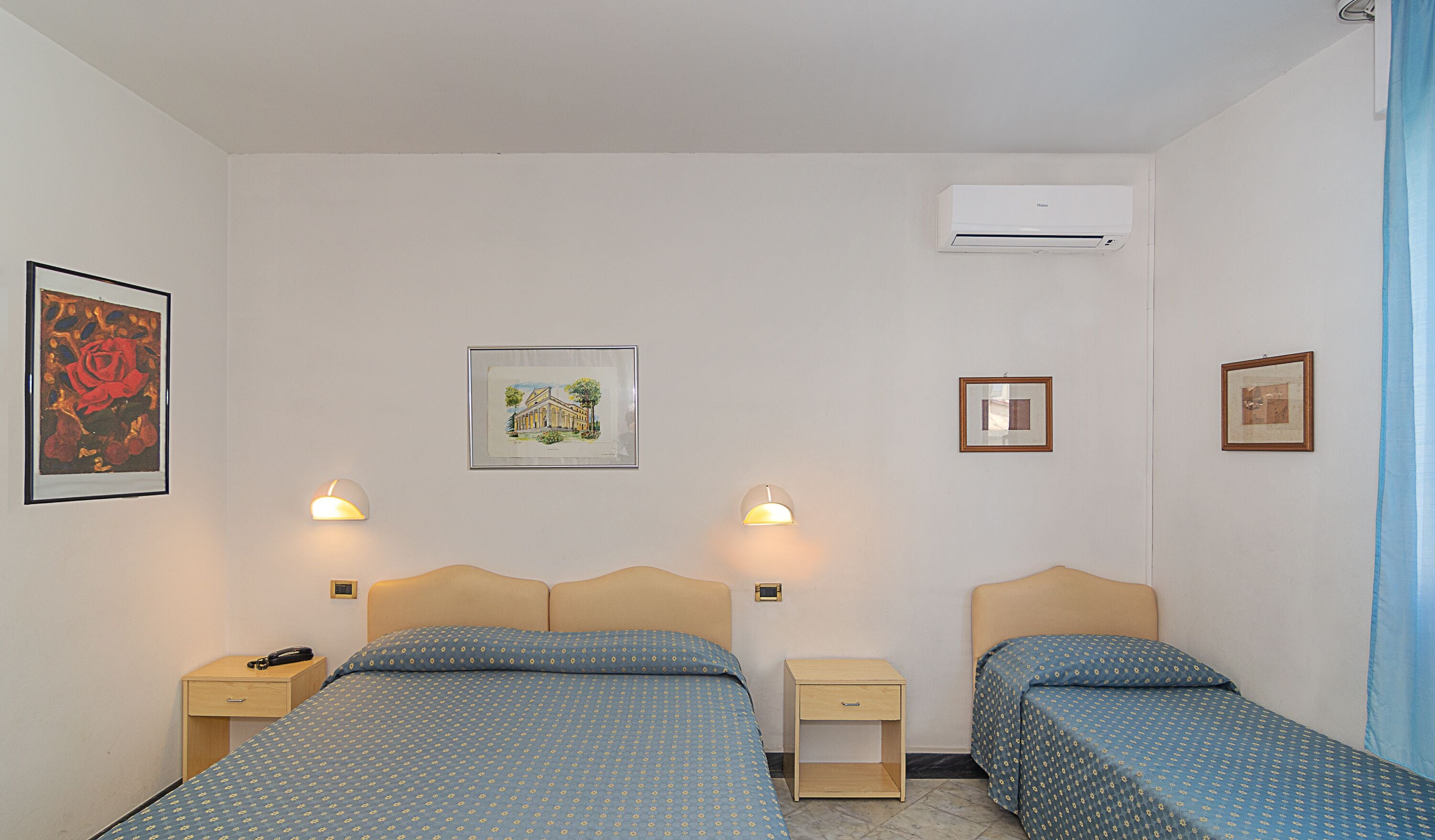 Ein Hotelzimmer mit zwei Betten, einem Nachttisch, einer Lampe und gerahmten Bildern an der Wand.