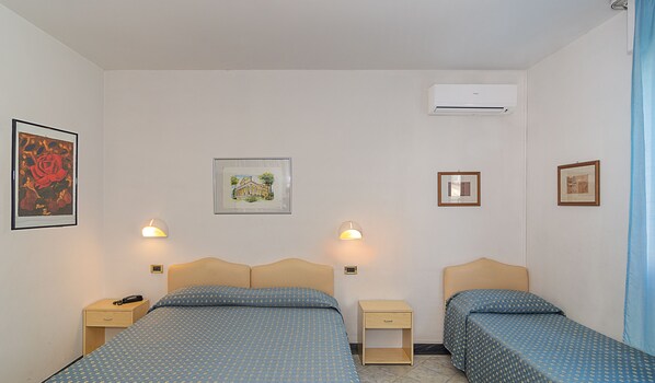 A hotel room with two beds, a nightstand, a lamp, and framed pictures on the wall. - Hotel Mariotti (Camaiore)