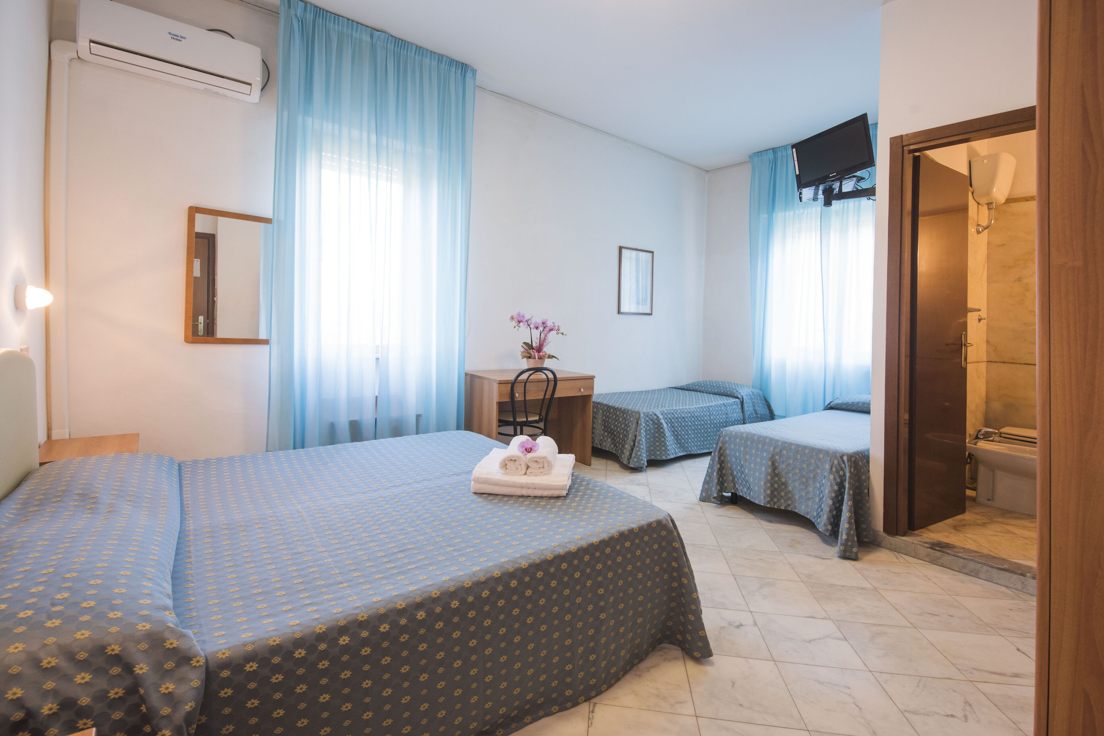 A hotel room with two beds, a desk, a chair, and a shower area.