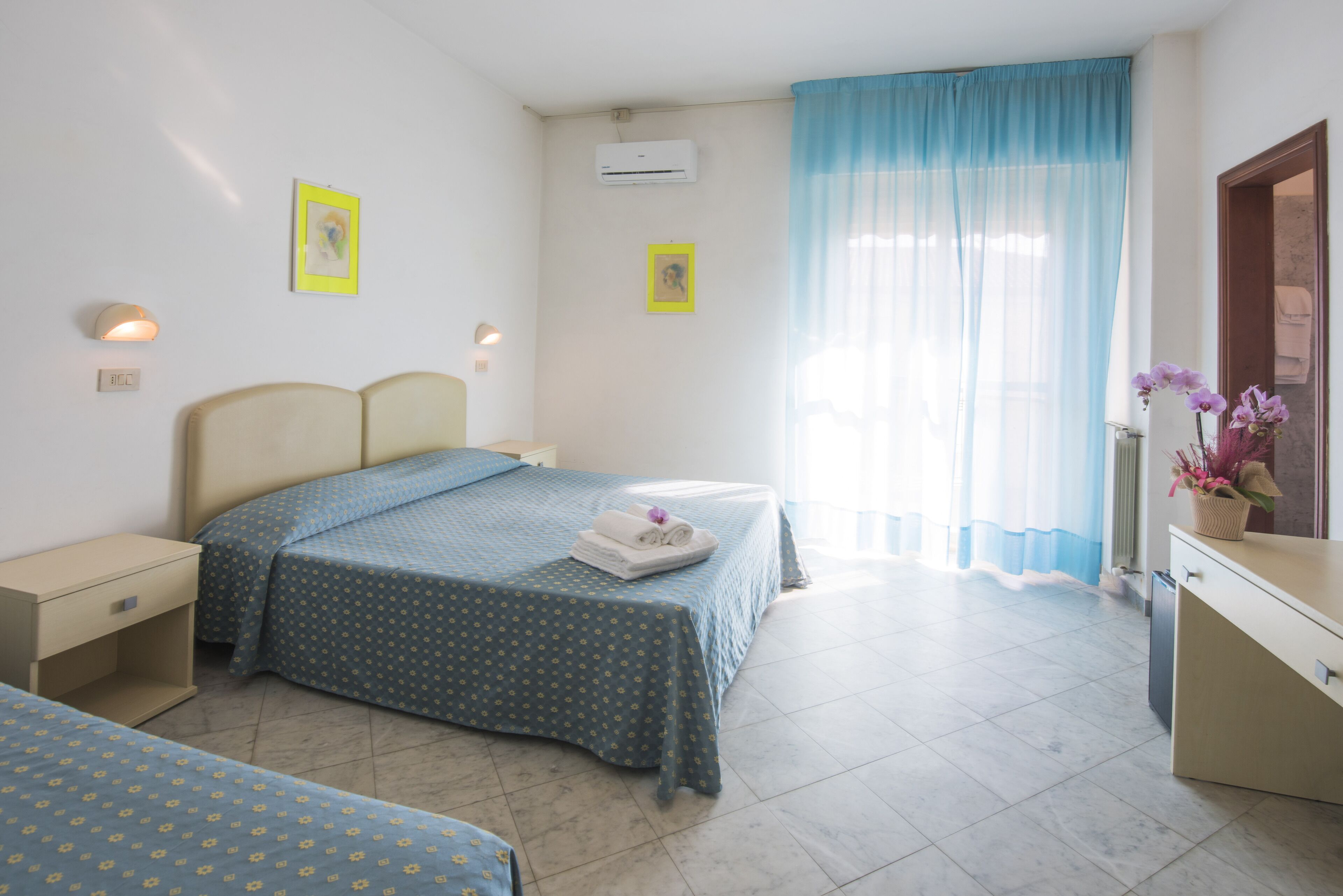 A hotel room with a bed, bedside tables, a desk, and a bathroom with a mirror and sink.